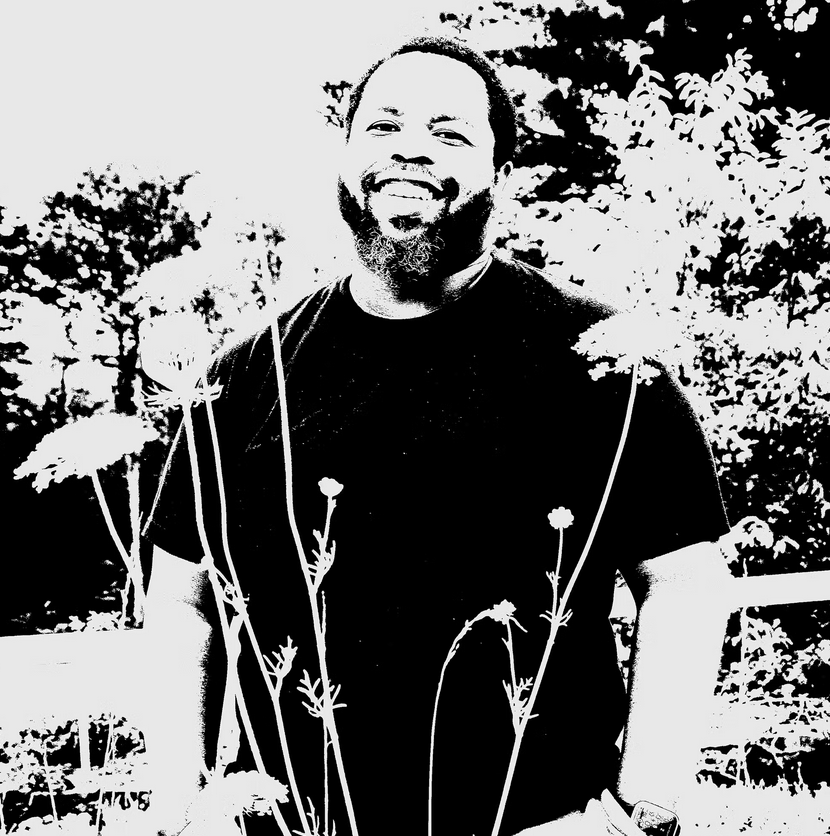 Ashton Crawley smiles at the camera while standing in a flower pasture and wearing a dark t-shirt.