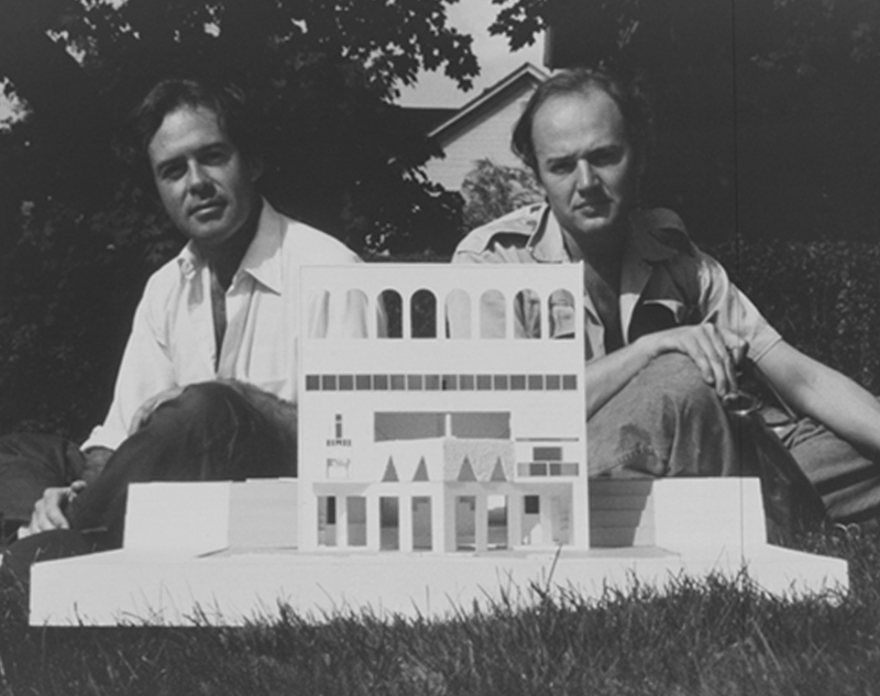 black and white image of rodolfo machado and jorge silvetti sitting next to their fountain house model outside in the grass.