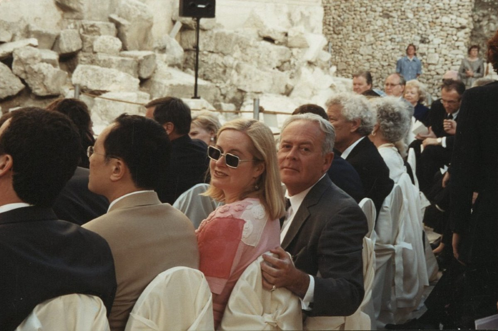 Rodolfo Machado and Brook Hodge look back at the camera while sitting at a ceremony.
