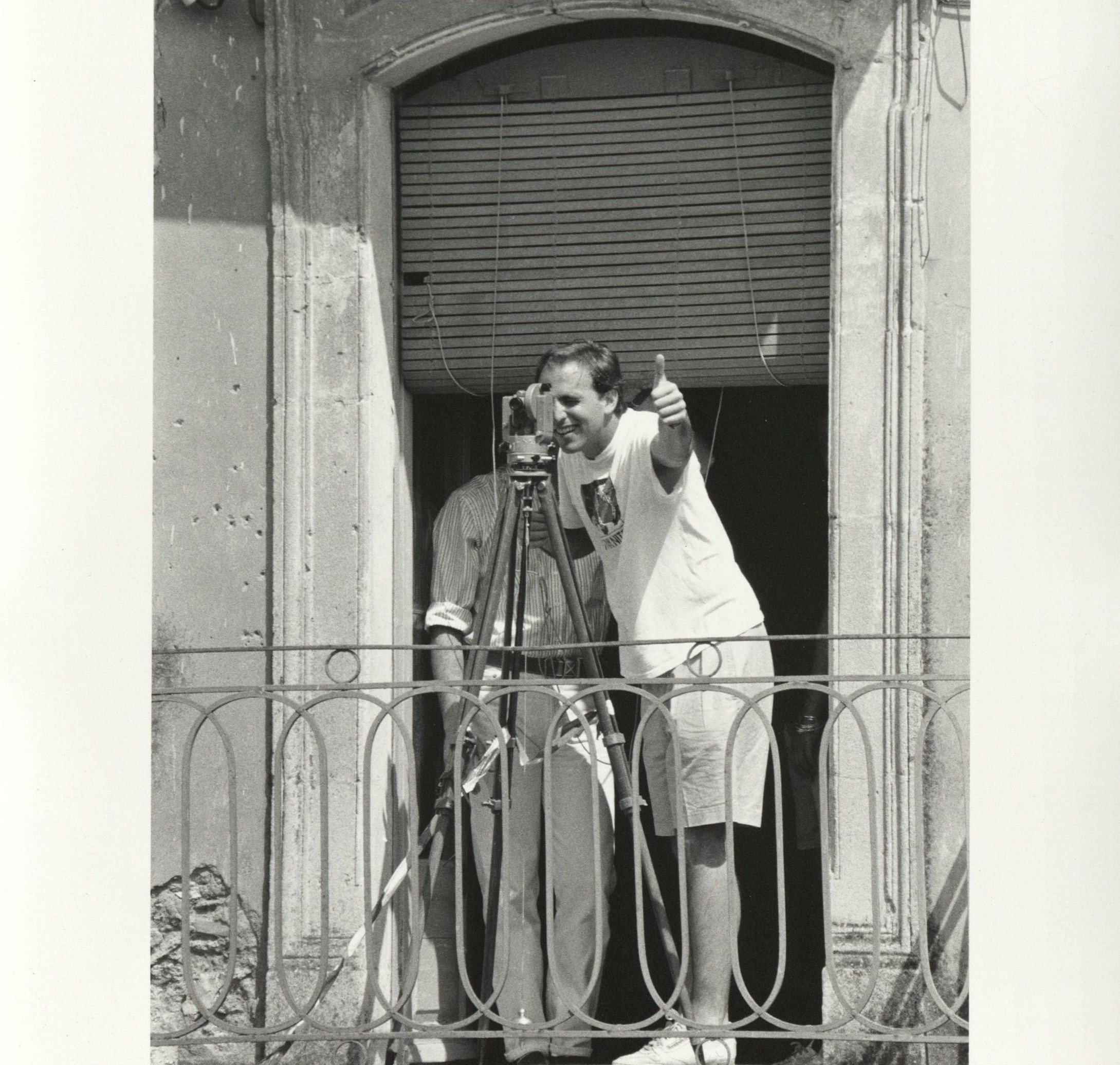 Two students stand on a balcony in Sicily while one looks into their own camera and gives a thumbs up.