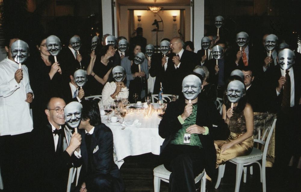 Group of people sit around a table and hold up Jorge Silvetti masks.